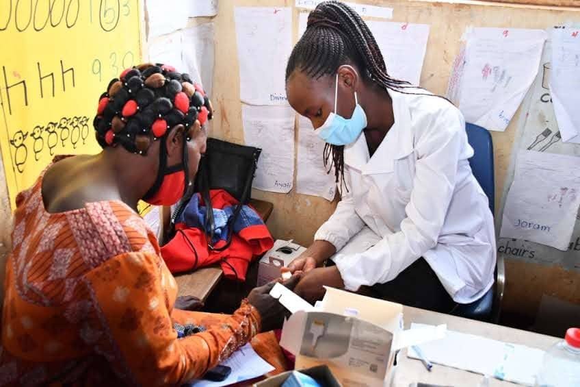 Health worker conducting an HIV screening in a classroom, with educational materials on the walls